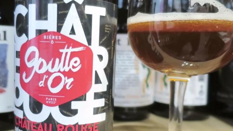 Eine Bierflasche mit dem Schriftzug "Goutte d'Or / Chateau Rouge" steht neben einem Glas Bier.
