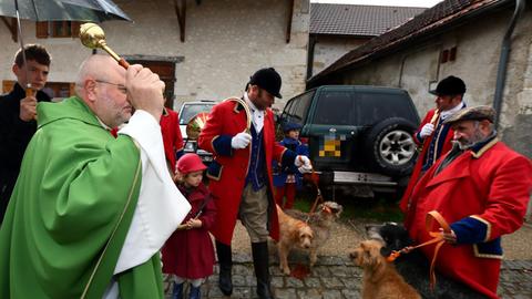 Eine Messe für den Schutzpatron der Jäger, Saint Hubert, in Injoux Génissiat, Frankreich. Ein Priester segnet eine Gruppe Jäger und ihre Jagdhunde in einem Hof.