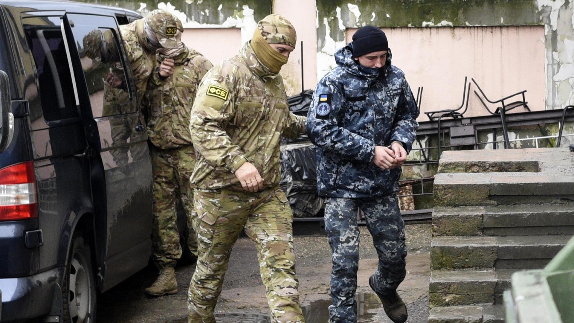 Zu sehen ist ein ukrainischer Marinesoldat, der in Handschellen von einem Offizier des russischen Nachrichtendienstes FSB zu einem Gerichtssaal begleitet wird. Zu sehen ist ein ukrainischer Marinesoldat, der in Handschellen von einem Offizier des russischen Nachrichtendienstes FSB zu einem Gerichtssaal begleitet wird.
