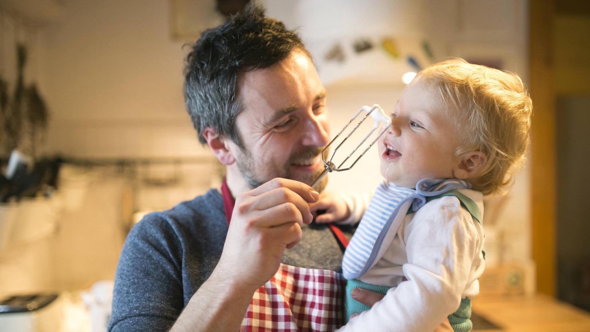 Ein lachender Vater mit kleinem Kind auf dem Arm in der Küche. Ein lachender Vater mit kleinem Kind auf dem Arm in der Küche.