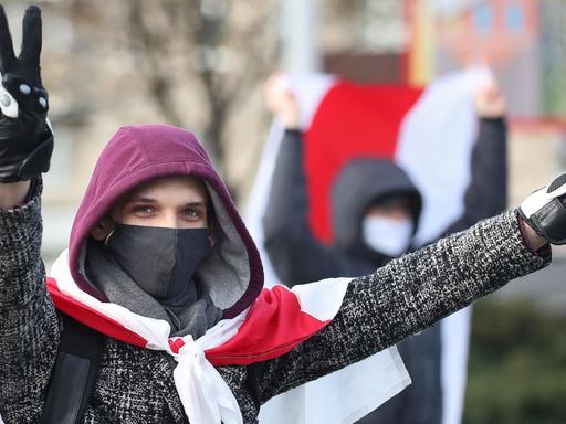 Ein junger Mann hat sich die rot-weiße Flagge als Cape umgebunden und formt mit beiden Händen ein Victory-Zeichen.