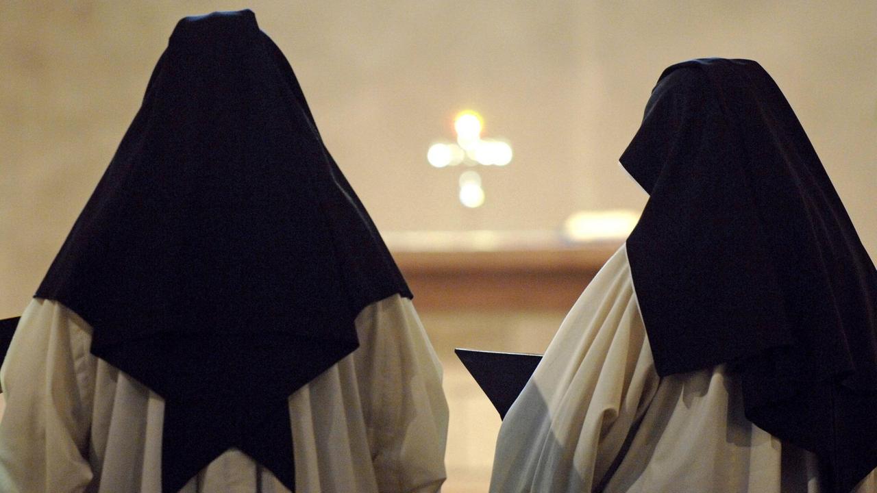 Zwei Zisterzienserinnen stehen im Kloster Lichtenthal in Baden-Baden bei der Messe mit dem Rücken zur Kamera. Sie tragen ein weißes Gewand und einen schwarzen Nonnenschleier. Zwei Zisterzienserinnen stehen im Kloster Lichtenthal in Baden-Baden bei der Messe mit dem Rücken zur Kamera. Sie tragen ein weißes Gewand und einen schwarzen Nonnenschleier.