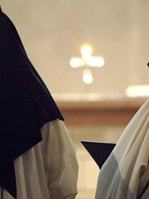 Zwei Zisterzienserinnen stehen ein einem Kloster in Deutschland bei der Messe mit dem Rücken zur Kamera. Sie tragen ein weißes Gewand und einen schwarzen Nonnenschleier. 