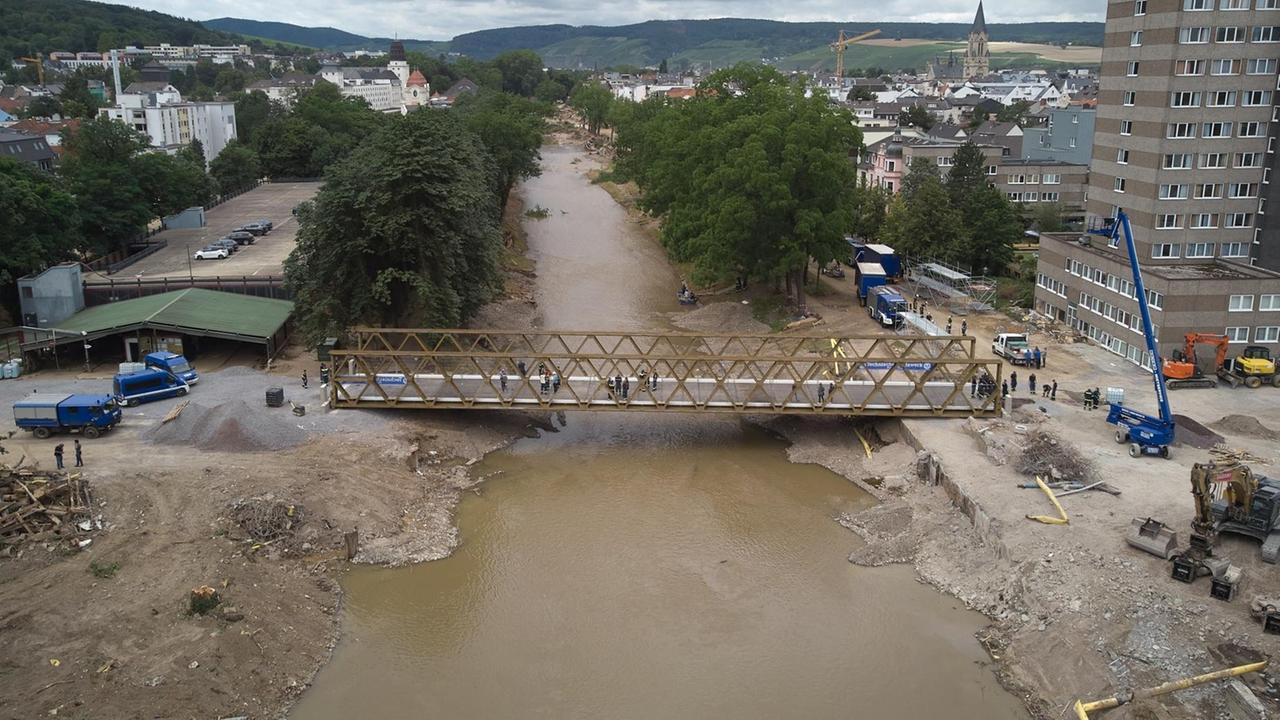 Eine Behelfsbrücke führt dort, wo in Bad Neuenahr die Markgrafenbrücke von der Flut zerstört wurde, über den Fluss. Links und rechts Bauschutt und Straßen mit Kieselbelag. Eine Behelfsbrücke führt dort, wo in Bad Neuenahr die Markgrafenbrücke von der Flut zerstört wurde, über den Fluss. Links und rechts Bauschutt und Straßen mit Kieselbelag.