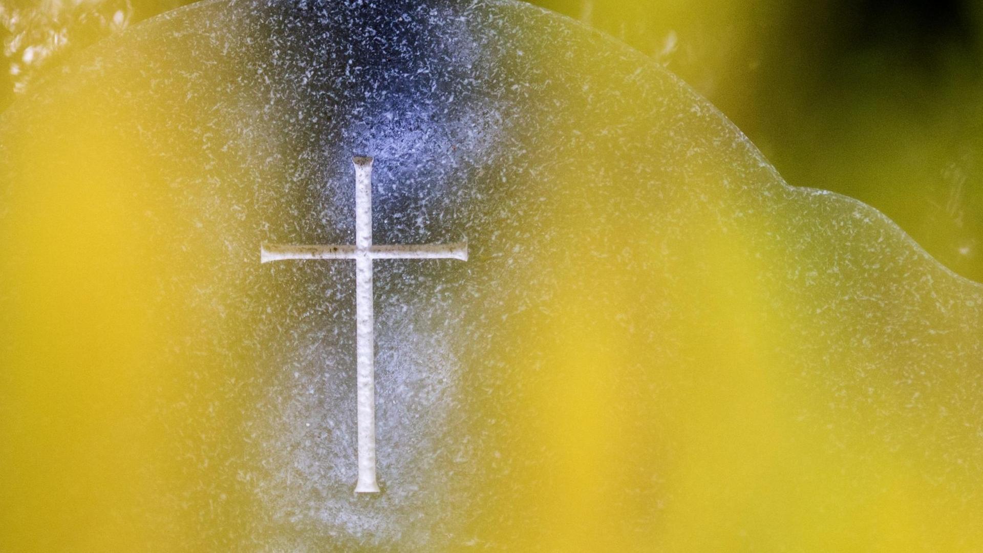 Ein Grabstein mit eingraviertem Kreuz steht am 22.10.2015 hinter einem gelben Grabgesteck auf einem Friedhof.