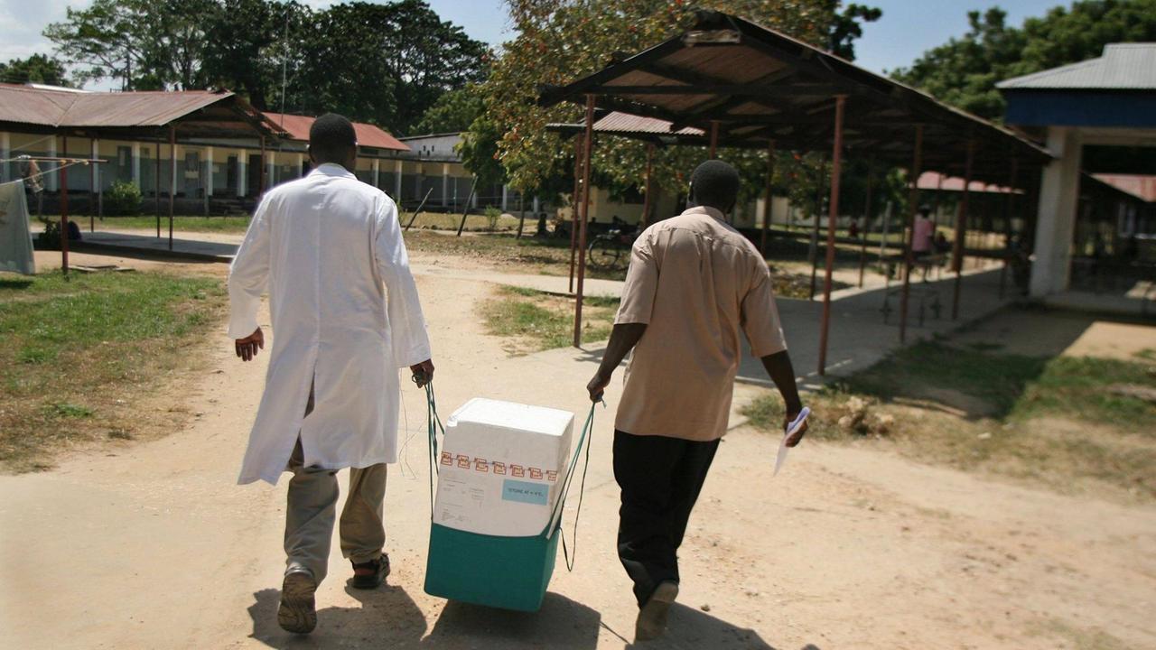Zwei Männer tragen einen Kühlbehälter mit Impfstoff vom Kühlhaus zum Ort der Impfung.  Bagamoyo, Tanzania, 2007  