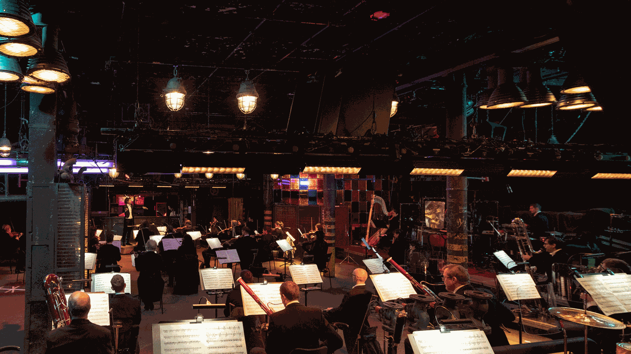 Das Orchester sitzt in einem Industrieraum und spielt nach Vorgabe seines Dirigenten. Das Orchester sitzt in einem Industrieraum und spielt nach Vorgabe seines Dirigenten.