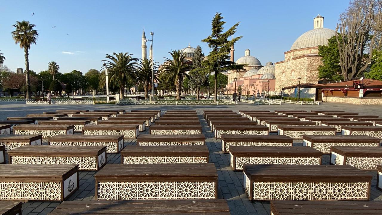 Unzählige leere symmetrisch aufgestellte Holzbänke stehen auf einem von Palmen umrandeten Platz. Im Hintergrund kann man die Hagia Sophia erkennen. Unzählige leere symmetrisch aufgestellte Holzbänke stehen auf einem von Palmen umrandeten Platz. Im Hintergrund kann man die Hagia Sophia erkennen.