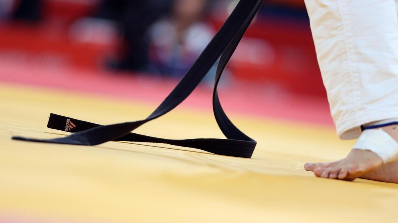 Ein schwarzer Judogürtel liegt zum Teil auf dem Boden Ein schwarzer Judogürtel liegt zum Teil auf dem Boden