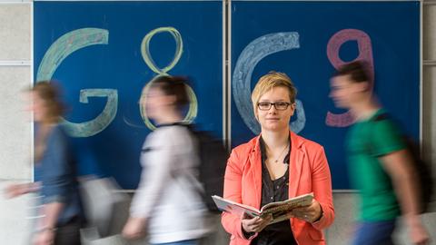 Gymnasiallehrerin Theresa Neudecker sitzt in einem Gymnasium in Straubing / Bayern vor einer Tafel mit der Aufschrift "G8" und "G9".