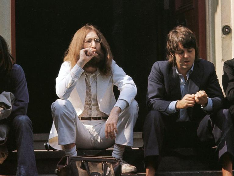 Die Beatles sitzen auf einer Treppe und gucken unverwandt in verschiedene Richtungen.