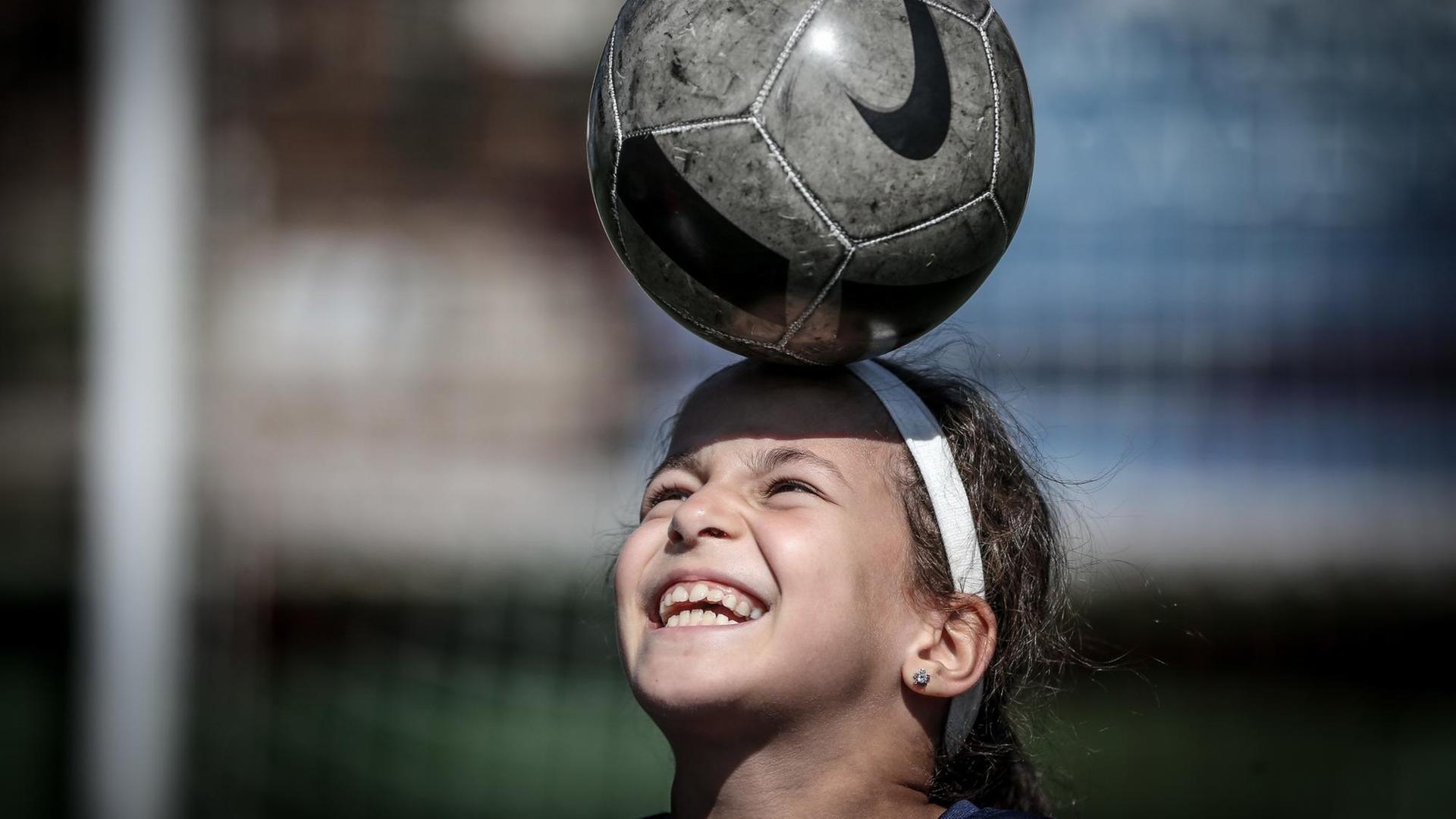 Ein 9-jähriges Mädchen balanciert einen Fußball auf dem Kopf. Ein 9-jähriges Mädchen balanciert einen Fußball auf dem Kopf.