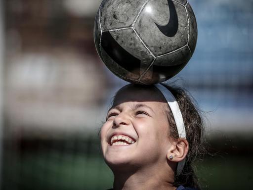 Ein 9-jähriges Mädchen balanciert einen Fußball auf dem Kopf.