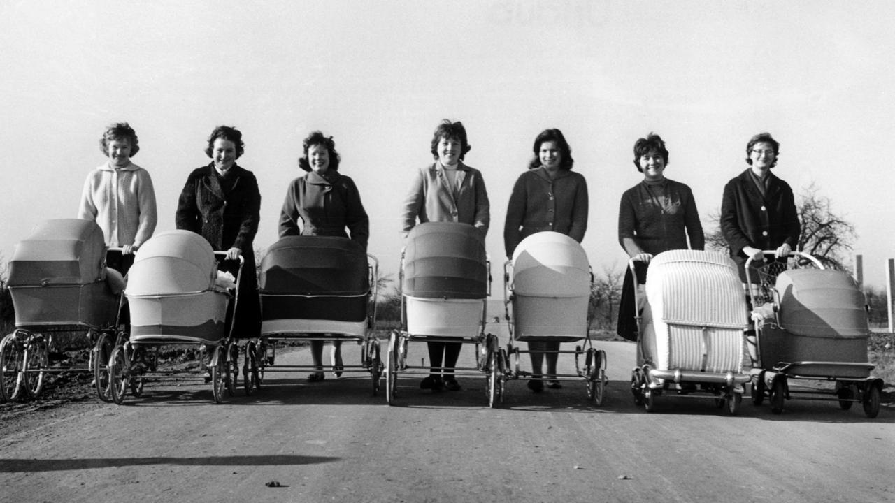 Sieben junge Mütter unternehmen am 01.03.1961 mit ihren Kinderwagen einen Frühlingsspaziergang auf einer asphaltierten Autostraße. 