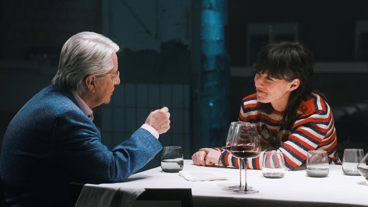 Zu sehen ist ein Mann, der mit einer Frau an einer Tafel sitzt. Beide unterhalten sich. Zu sehen ist ein Mann, der mit einer Frau an einer Tafel sitzt. Beide unterhalten sich.
