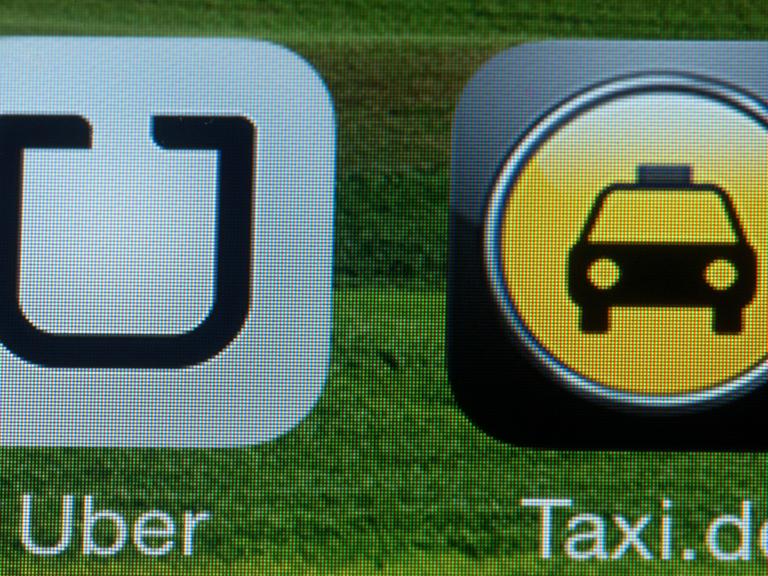 Die Handy-App "Uber" auf einem Smartphone neben dem Logo der Taxi-Vermittlung, Aufnahme vom September 2014