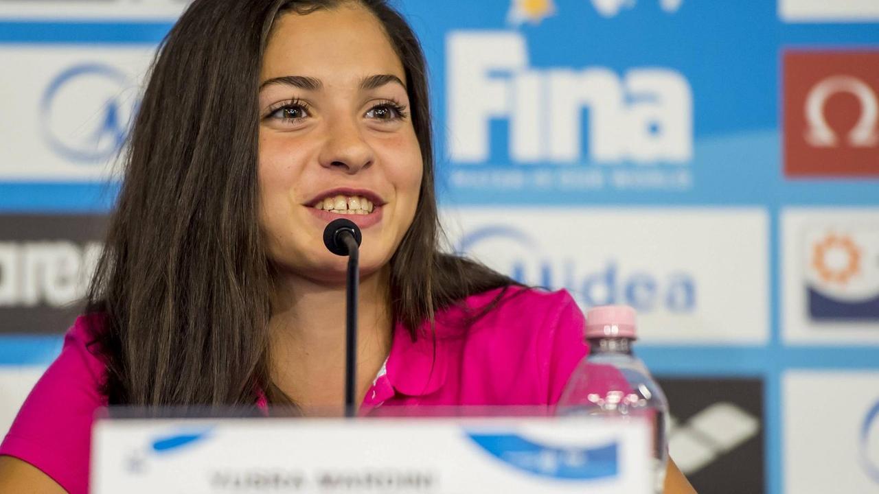 Yusra Mardini sitzt auf einem Podium und spricht in ein Mikrofon. Yusra Mardini sitzt auf einem Podium und spricht in ein Mikrofon.