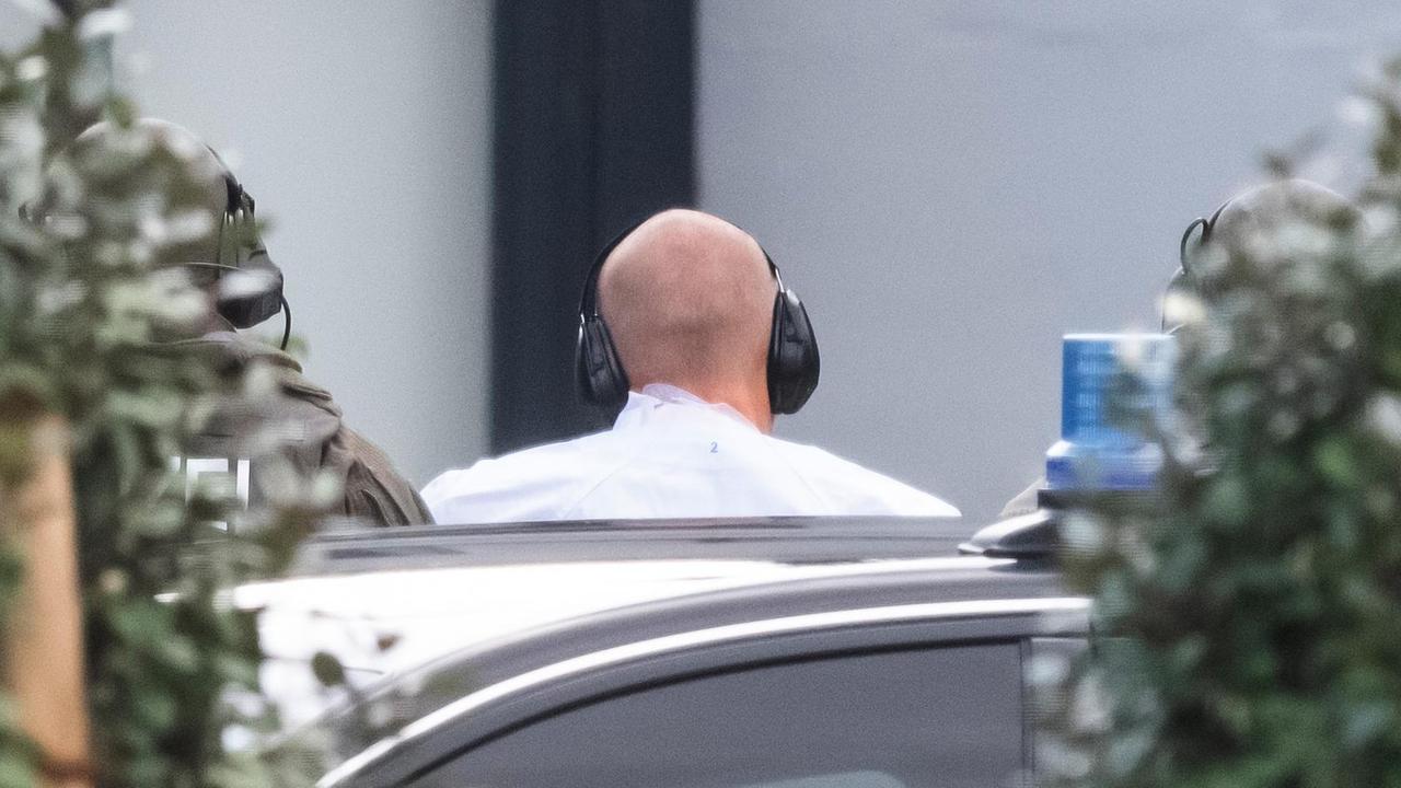Der Tatverdächtige von Halle wird zur Außenstelle des Bundesgerichtshofs gebracht. Zu sehen ist ein kahler Hinterkopf von hinten mit Ohrenschützern.