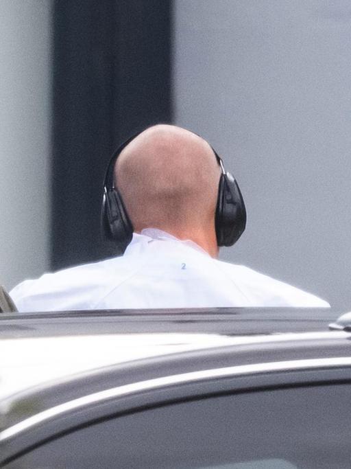 Der Tatverdächtige von Halle wird zur Außenstelle des Bundesgerichtshofs gebracht. Zu sehen ist ein kahler Hinterkopf von hinten mit Ohrenschützern.