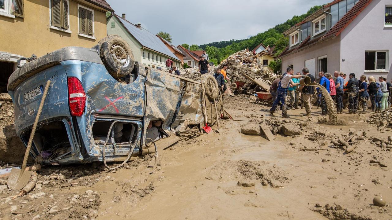 Helfer bilden am 04.06.2016 in Braunsbach (Baden-Württemberg) eine Menschenkette, um möglichst viel Schlamm mit Eimern aus einem Haus im Ort zu bekommen, während davor ein Auto auf dem Dach liegt. Helfer bilden am 04.06.2016 in Braunsbach (Baden-Württemberg) eine Menschenkette, um möglichst viel Schlamm mit Eimern aus einem Haus im Ort zu bekommen, während davor ein Auto auf dem Dach liegt.