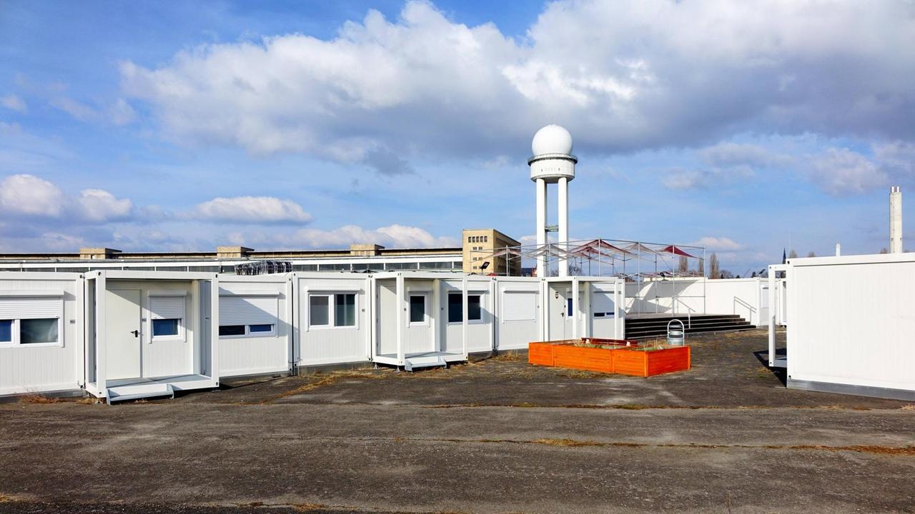 Das Foto zeigt das als Flüchtlingsunterkunft dienende Containerdorf auf dem Tempelhofer Feld. Im Vordergrund die Container, im Hintergrund der ehemalige Tower des Flughafens.