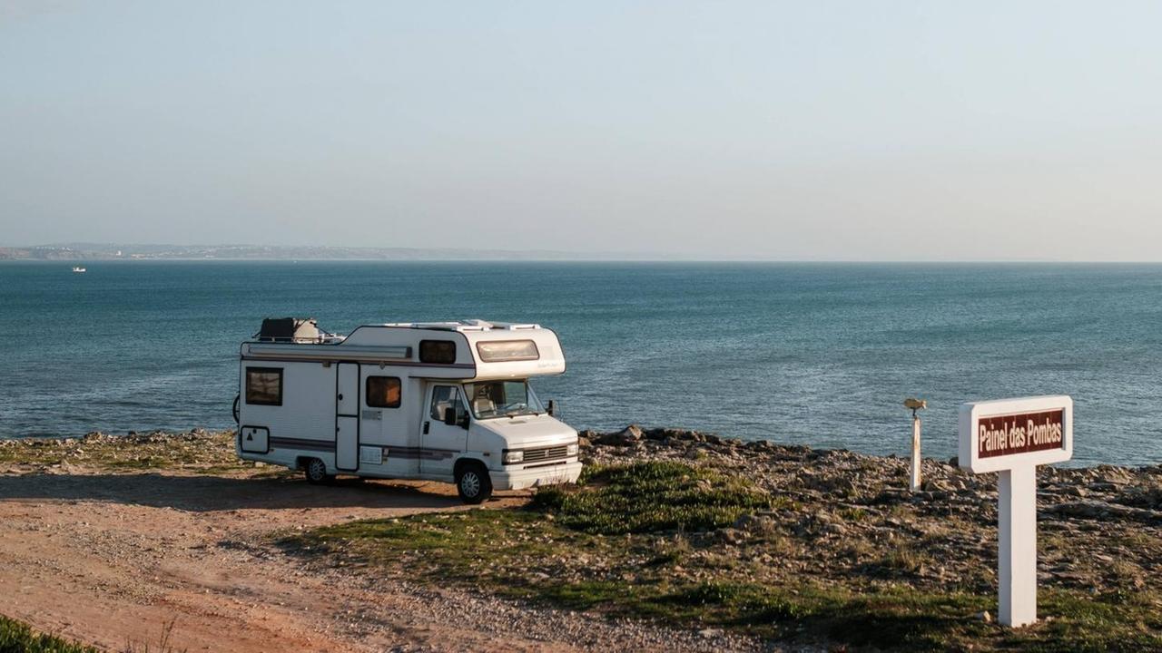 Ein Camper-Van steht auf einem Parkplatz am Meer. Ein Camper-Van steht auf einem Parkplatz am Meer.