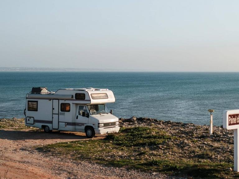Ein Camper-Van steht auf einem Parkplatz am Meer.
