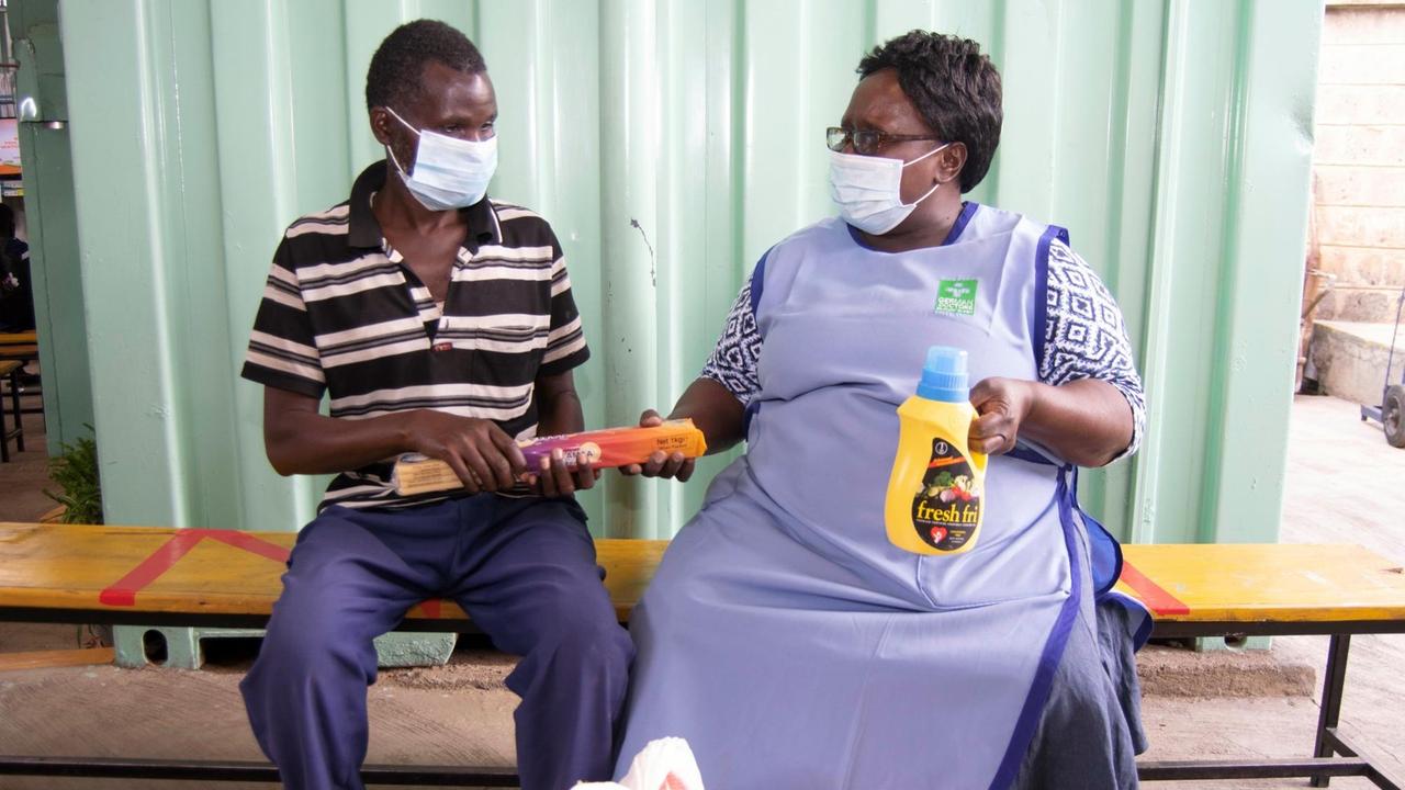 Ein blinder Mann erhält im Ernährungszentrum im Slum Mathare von einer German Doctors-Mitarbeiterin Nahrungsmittel überreicht