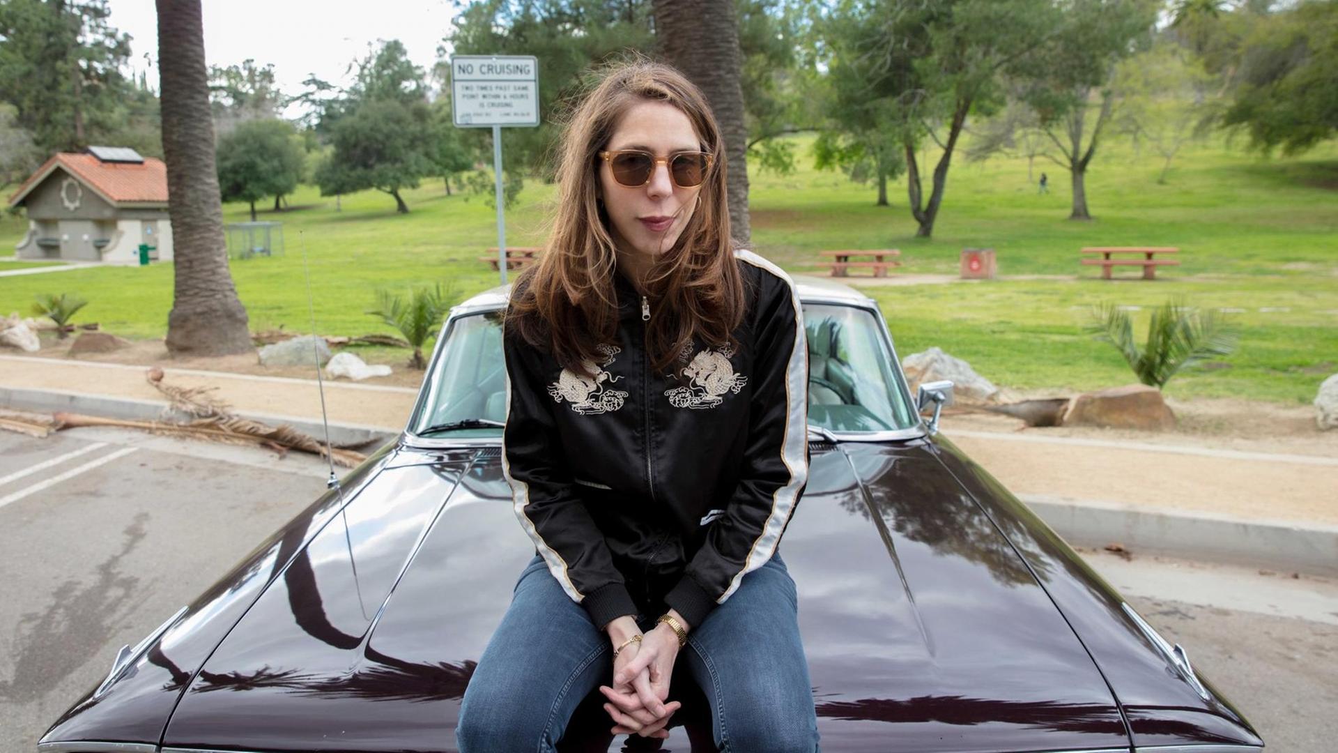 Rachel Kushner sitzt auf der Motorhaube eines us-amerikanischen Sportwagens. Sie trägt eine Sonnenbrille. Rachel Kushner sitzt auf der Motorhaube eines us-amerikanischen Sportwagens. Sie trägt eine Sonnenbrille.