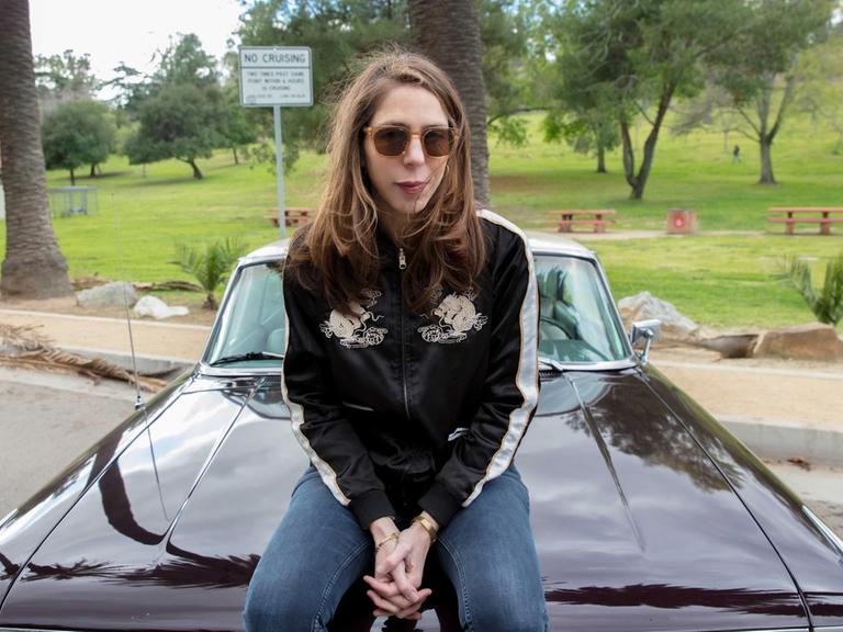 Rachel Kushner sitzt auf der Motorhaube eines us-amerikanischen Sportwagens. Sie trägt eine Sonnenbrille.