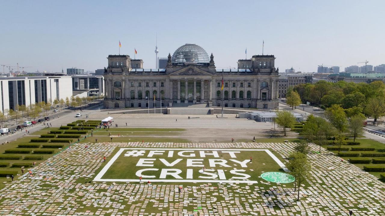 Zahlreiche Protestschilder liegen auf der Wiese vor dem Bundestag – dazwischen steht "#Fight Every Crisis". Zahlreiche Protestschilder liegen auf der Wiese vor dem Bundestag – dazwischen steht "#Fight Every Crisis".