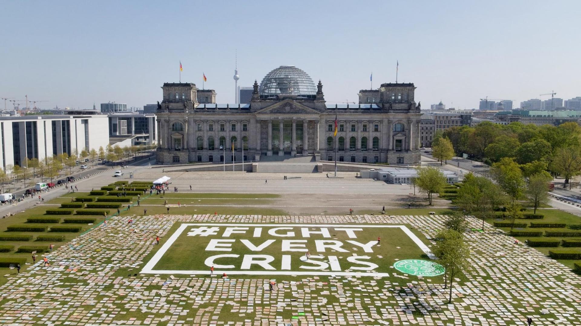 Zahlreiche Protestschilder liegen auf der Wiese vor dem Bundestag – dazwischen steht "#Fight Every Crisis". Zahlreiche Protestschilder liegen auf der Wiese vor dem Bundestag – dazwischen steht "#Fight Every Crisis".