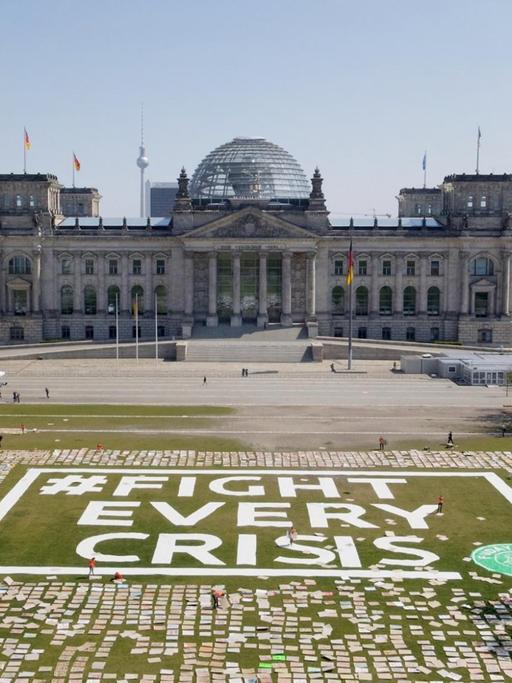 Zahlreiche Protestschilder liegen auf der Wiese vor dem Bundestag – dazwischen steht "#Fight Every Crisis".