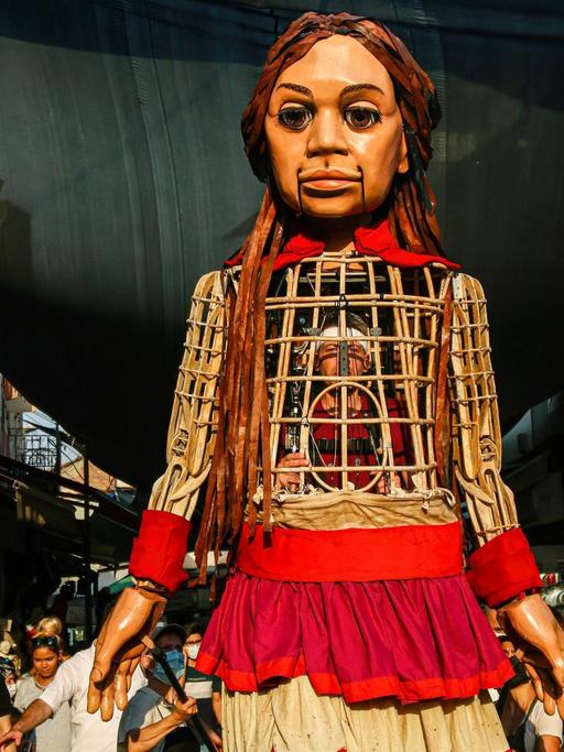 Die 3,5 Meter große Puppe "Amal" läuft durch die Straßen desr türkischen Stadt Izmir. Sie ist ein Teil der Kunstaktion "The Walk", in Gaziantepp gestartet und wird vier Monate lang 8.000 Kilometer gehen sowie acht Ländergrenzen der EU passieren. Dabei soll sie auf alle Herausforderungen aufmerksam machen, die syrische geflüchtete Kinder meistern müssen.