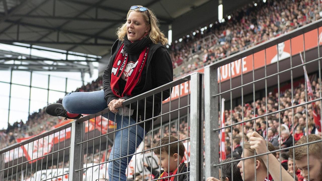 Eine Frau klettert beim Spiel des 1. FC Köln gegen Jahn Regensburg auf den Zaun zwischen Fanblock und Spielfeld.
