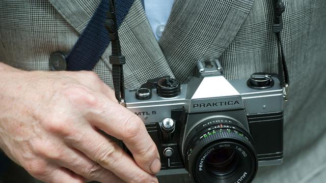 Eine alte Spiegelreflexkamera vom Typ Praktica MTL 5 hängt an einem Band vor einem Bauch.