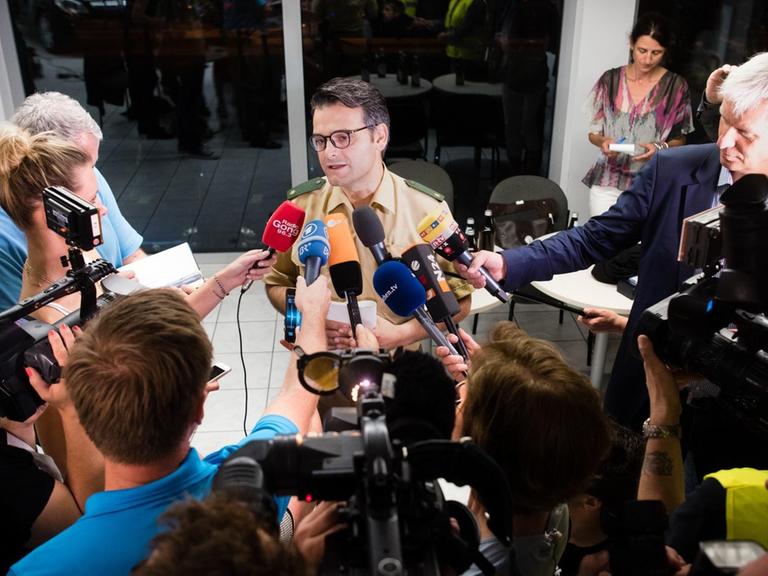 Sie sehen Marcus da Gloria Martins, den Pressesprecher der Polizei München, auf den viele Mikrofone gerichtet sind.