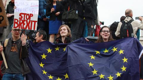 Am 28. Juni 2016 protestieren Briten gegen den EU-Austritt ihres Landes auf dem Trafalgar Square in London. Im Vordergrund sind zwei junge Frauen zu sehen, die EU-Flaggen hochhalten. Daneben hält ein junger Mann ein Schild mit der Aufschrift "Stop Brexit" in die Höhe.