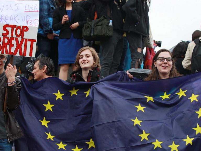Am 28. Juni 2016 protestieren Briten gegen den EU-Austritt ihres Landes auf dem Trafalgar Square in London. Im Vordergrund sind zwei junge Frauen zu sehen, die EU-Flaggen hochhalten. Daneben hält ein junger Mann ein Schild mit der Aufschrift "Stop Brexit" in die Höhe.