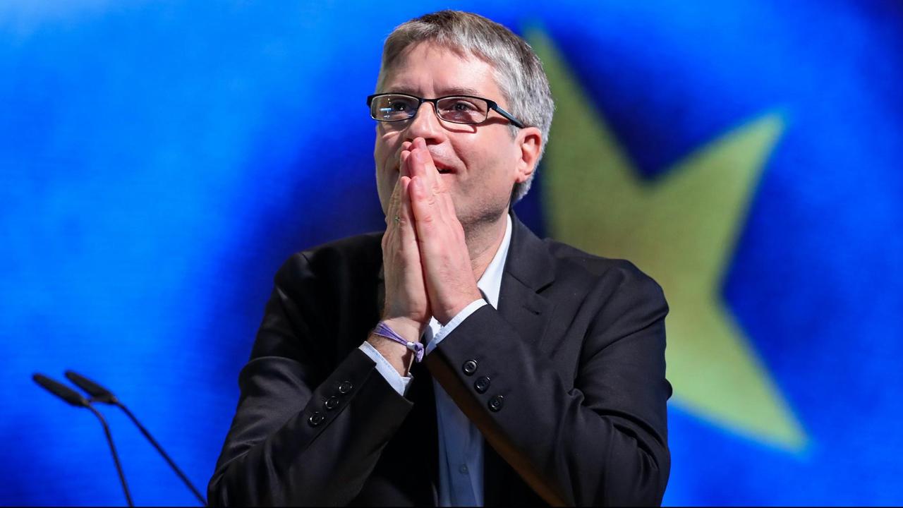 Sven Giegold hat die Hände vor dem Mund gefaltet, im Hintergrund ein Teil der Europa-Fahne.