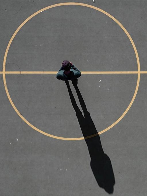 Ein Mann steht im Zentrum eines Spielfeldes, sein Schatten ragt aus dem Mittelkreis heraus.