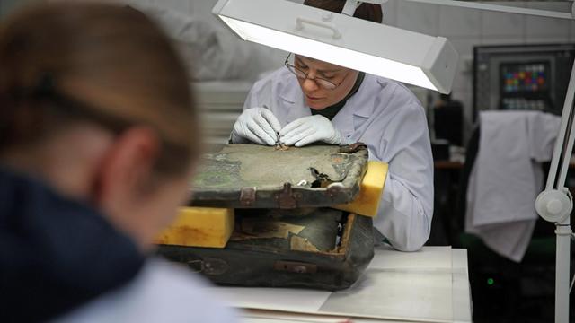 Die Konservatorin Margrit Bormann beugt sich in der Restaurationswerkstatt über den alten und beschädigten Koffer eines Holocaust-Opfers