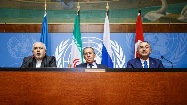 Die drei Politiker sitzen nebeneinander an einem erhöhten Pult mit Mikrofonen. Hinter ihnen die Flaggen ihrer Länder vor einer Wand mit dem UNO-Zeichen.