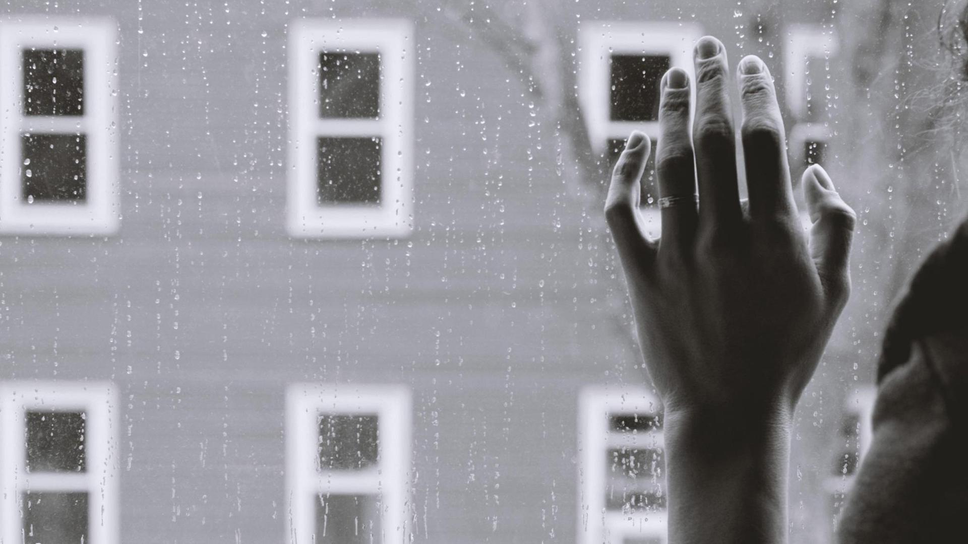 Eine Hand vor einem Fenster, dahinter Regen. Eine Hand vor einem Fenster, dahinter Regen.