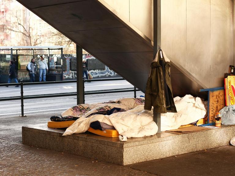 Obdachlose haben zwischen zwei Straßen unter einer Treppe ihr Lager errichtet.