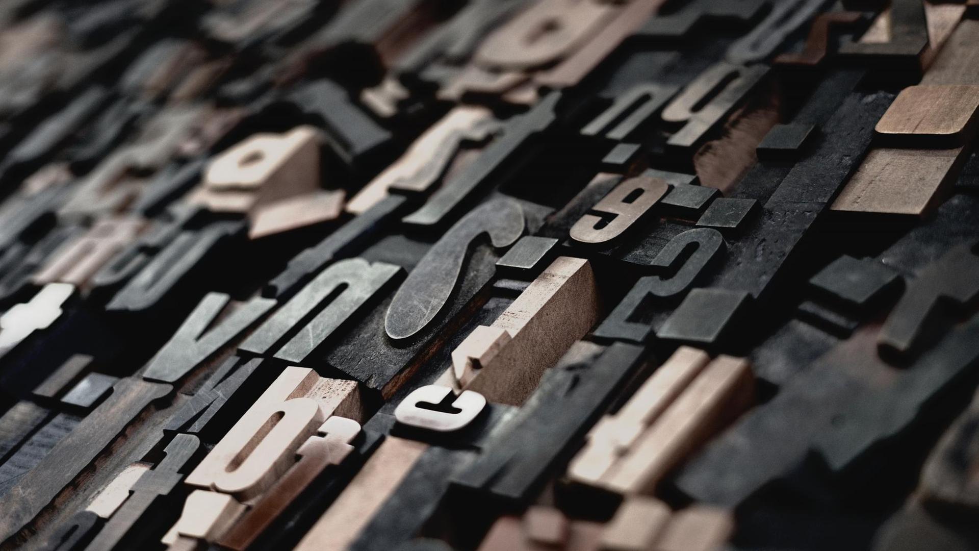 Einzelne, hölzerne Buchstaben liegen kreuz und quer bereit zum setzen der Texte im historischen Druckverfahren. Einzelne, hölzerne Buchstaben liegen kreuz und quer bereit zum setzen der Texte im historischen Druckverfahren.
