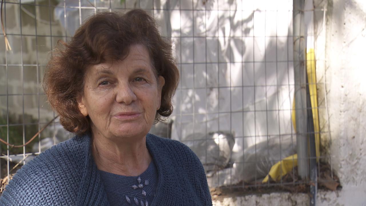 Eine burschikose ältere Frau mit kurzen welligen rötlich-braunen Haaren und in Wolljacke sitzt draußen an einer Ecke eines Hauses. Eine burschikose ältere Frau mit kurzen welligen rötlich-braunen Haaren und in Wolljacke sitzt draußen an einer Ecke eines Hauses.