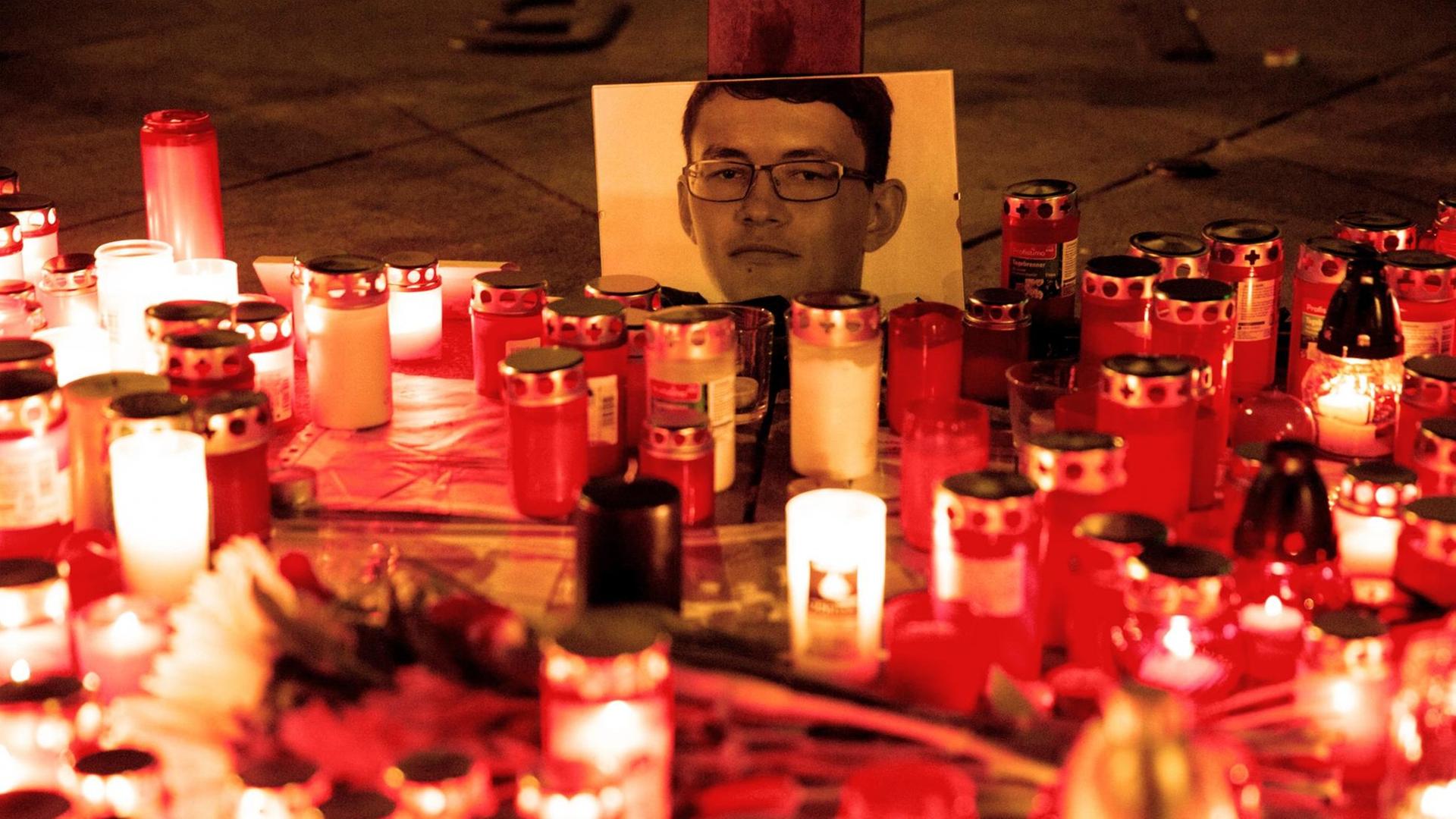Mehrere Dutzend Grabkerzen stehen erleuchtet vor einem Foto des ermordeten Journalisten Jan Kuciak