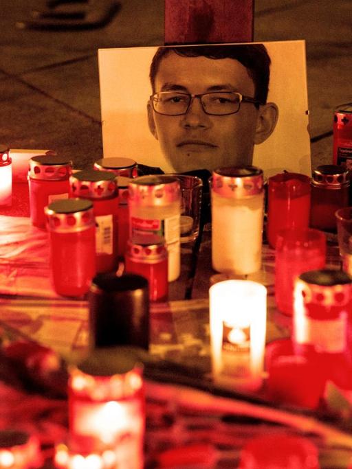 Mehrere Dutzend Grabkerzen stehen erleuchtet vor einem Foto des ermordeten Journalisten Jan Kuciak