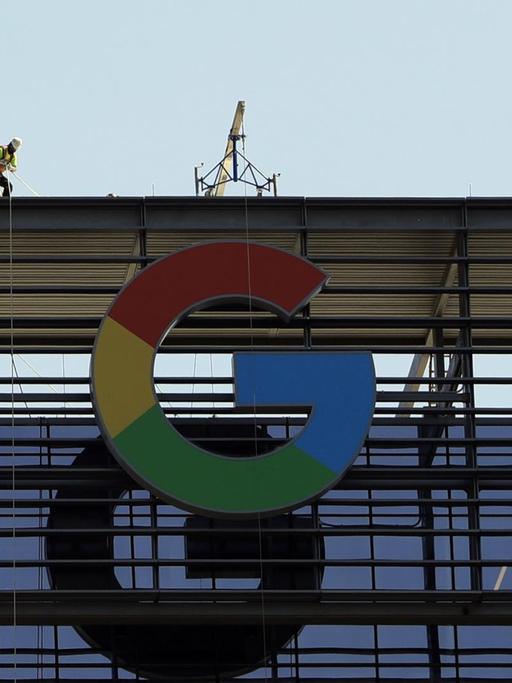 Bauarbeiter arbeiten auf einem Gebäude, an dem das große "G" für Google steht
